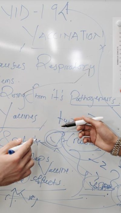 pexels photo 7869302 7869302 Hands holding markers writing notes on a whiteboard about COVID-19 and vaccination.